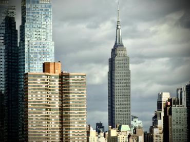 Empire State Building towering among city skyscrapers under a cloudy sky.