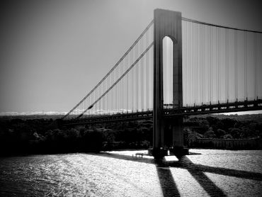 Black and white photo of a suspension bridge casting shadows on water.