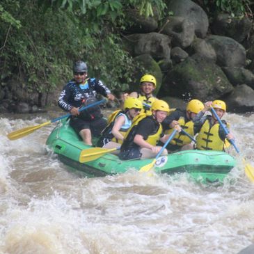 Group of six people white water rafting with yellow helmets and paddles.