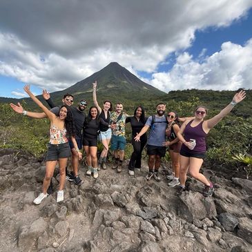 Group of friends posing happily in front of a volcano during a hike.