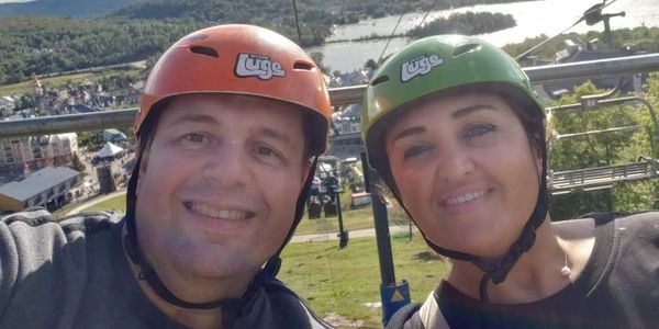 Two people wearing helmets smiling on a ski lift.