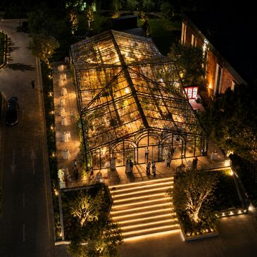 A beautifully lit glass greenhouse at night with illuminated stairs and surrounding greenery.