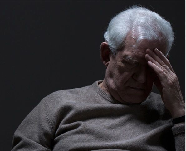 Elderly man looking distressed with hand on forehead.