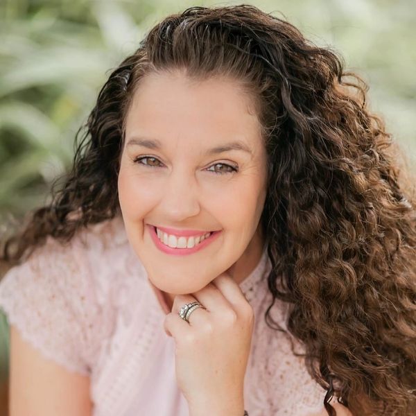 Smiling woman with curly hair resting her chin on her hand.