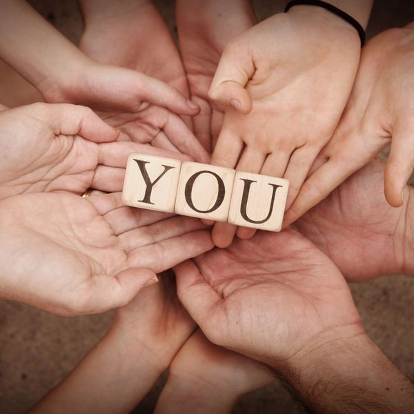 Multiple hands holding blocks spelling 'YOU' together.
