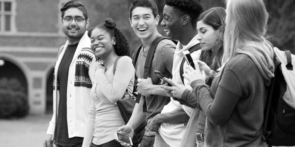 A diverse group of young adults laughing and using phones outdoors.