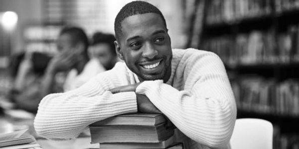 Smiling student leaning on books in a library.