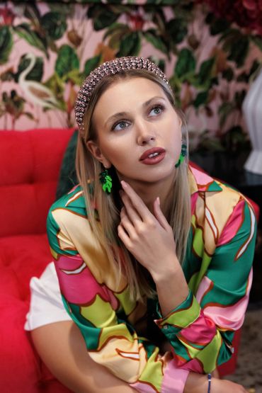 Young woman in colorful outfit sits thoughtfully on red couch.