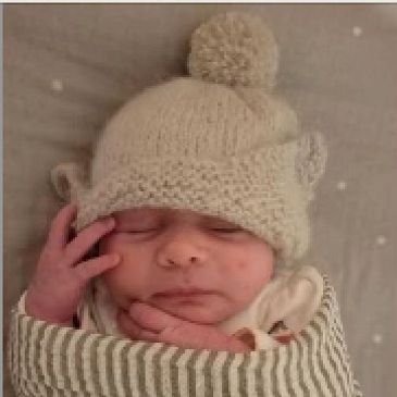Newborn baby wrapped in striped blanket wearing a knitted hat with ears and pom-pom.