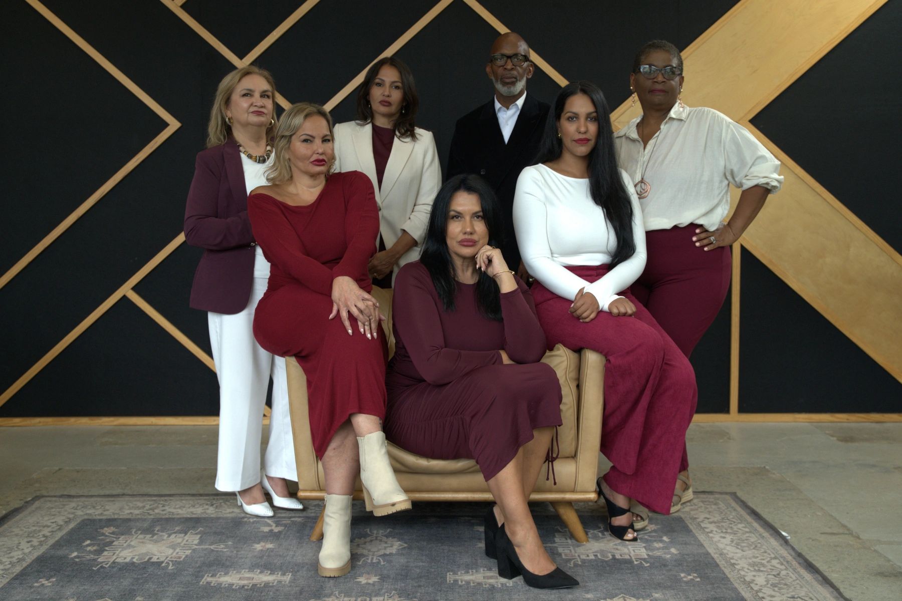 Group portrait of seven diverse professionals in stylish attire with a geometric backdrop.