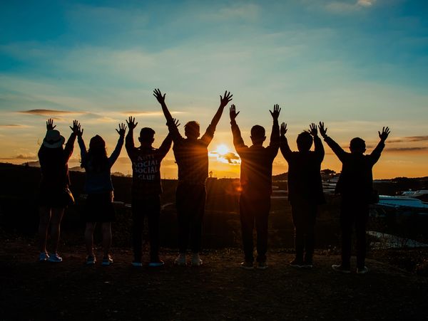 Silhouetted group raising hands at sunset outdoors.