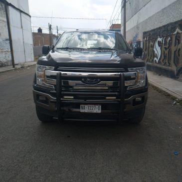 Front view of a black Ford truck with a protective grille on a quiet street.