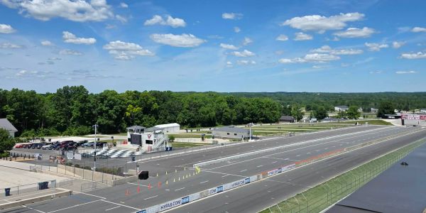 A wide drag racing track under a blue sky with scattered clouds.