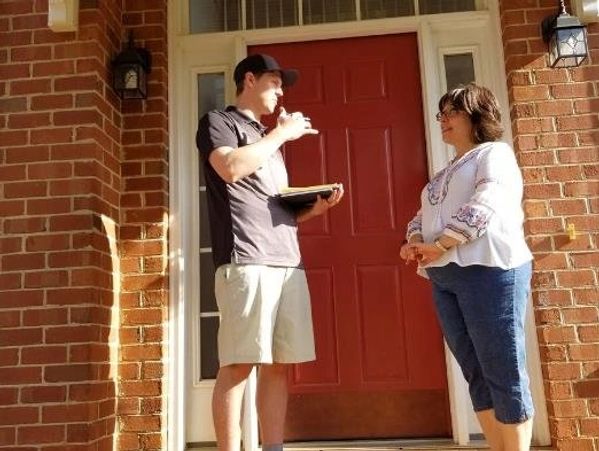 A sales person from Hail Inc talking to a woman in front of her house with red door. 