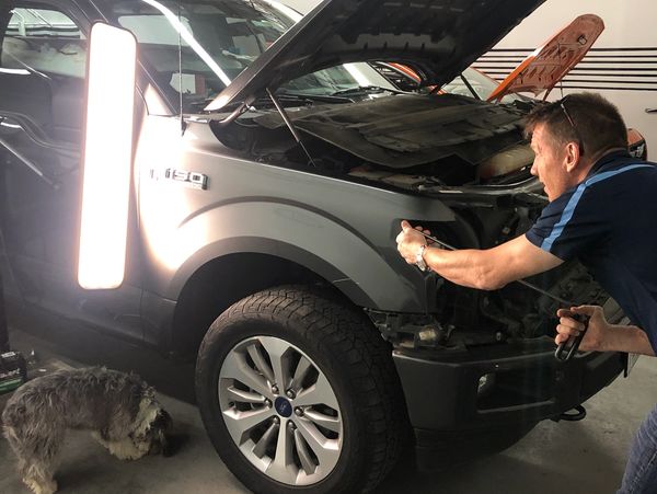 A man is fixing hail damage on a grey car. 