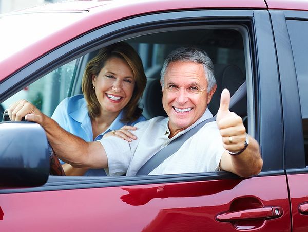 An older man and a woman in a red car, man is holding his thumb up. 