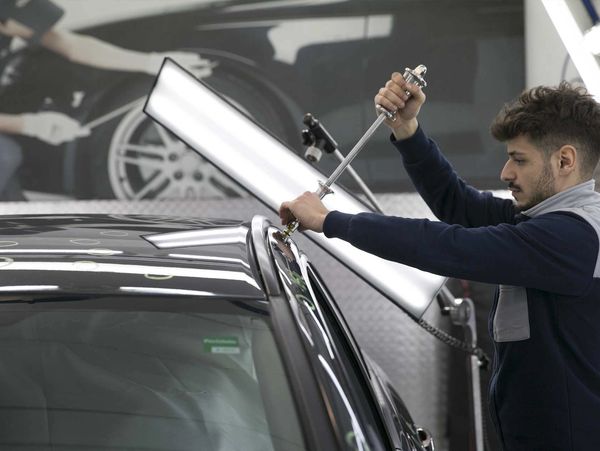 A man is fixing hail damage on a black car