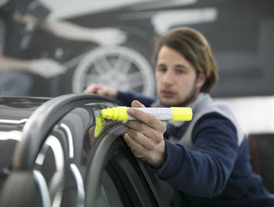 A man is circling hail damage on a black car with a yellow marker