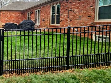 Black metal fence for puppy enclosing a backyard with a gazebo and covered grills.