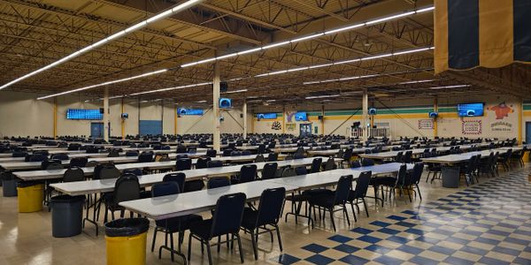 Large, empty cafeteria with rows of tables and chairs.