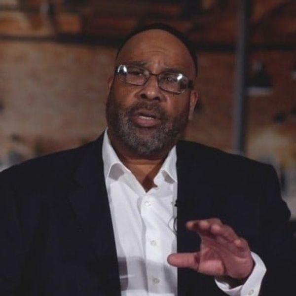 Man in suit speaking with a serious expression indoors.