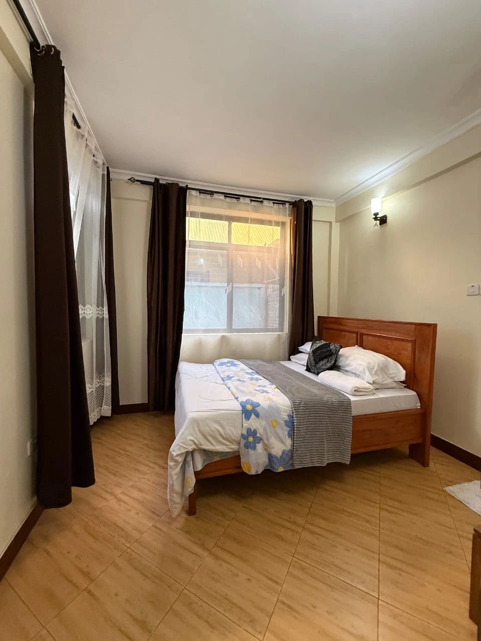 Cozy bedroom with wooden bed and floral bedding near a window with brown curtains.