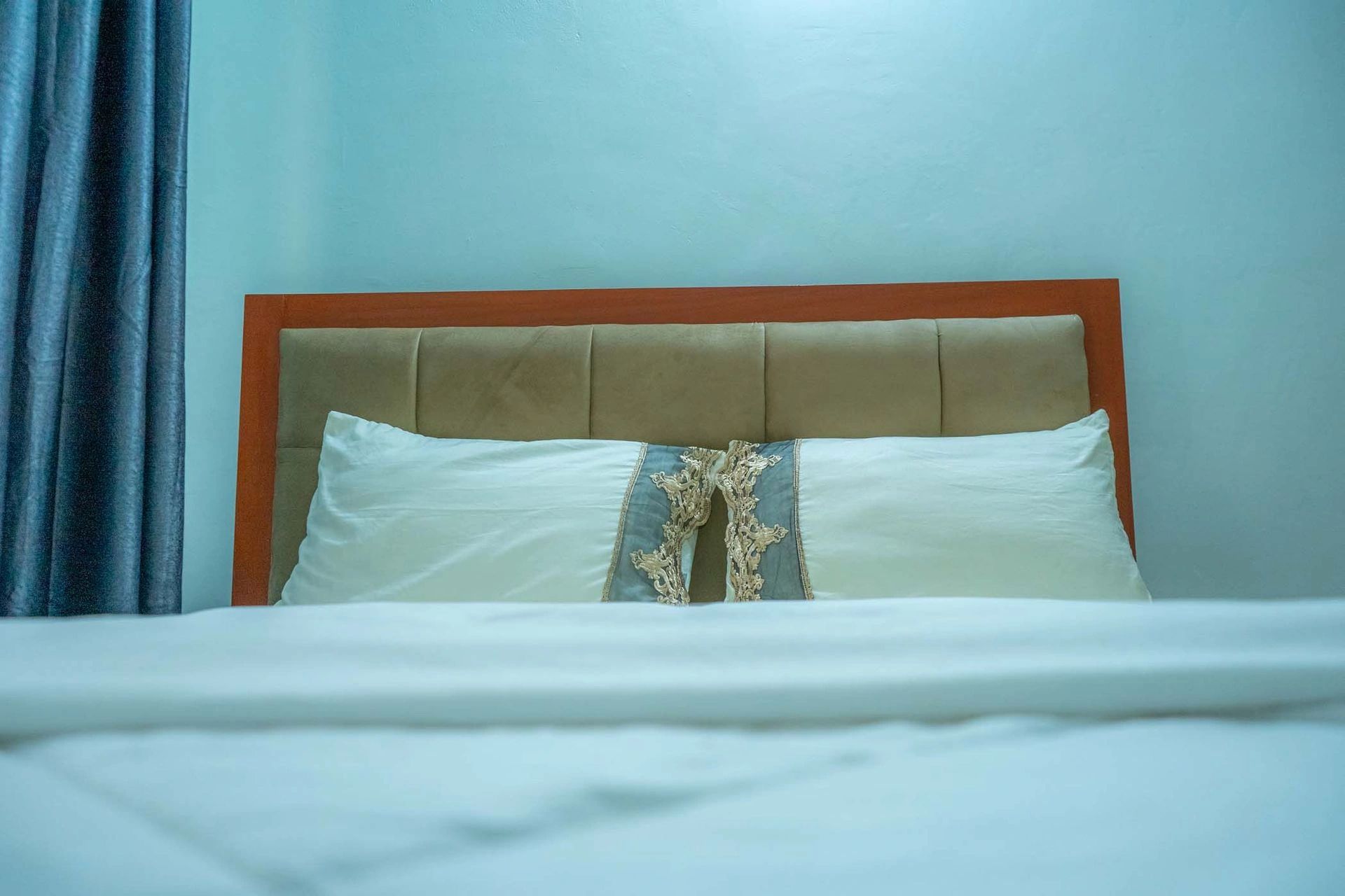 Close-up of a neatly made bed with decorative pillows and blue walls.