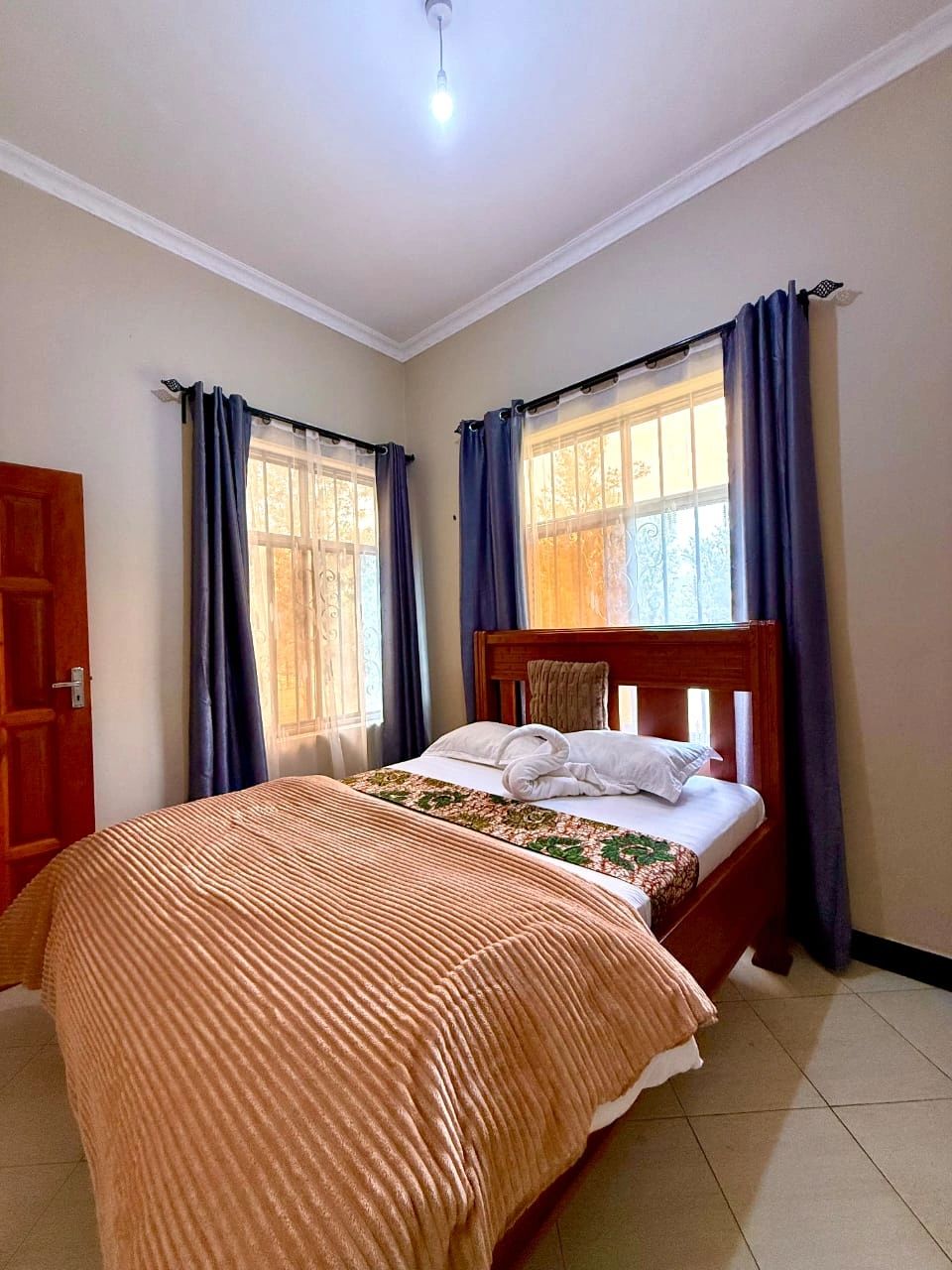 Cozy bedroom with wooden bed, beige blanket, and blue curtains.