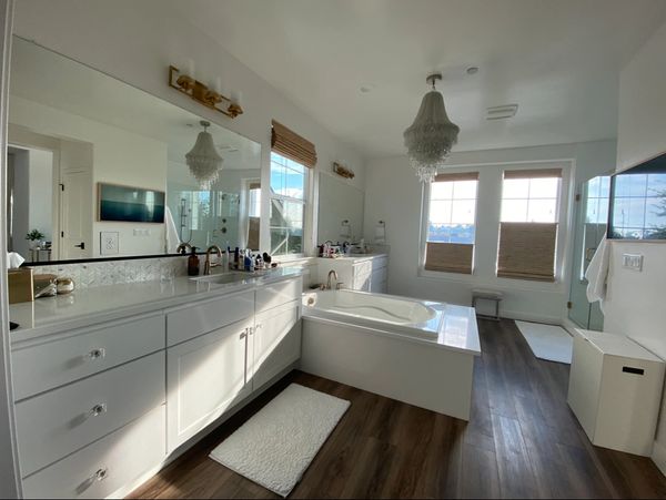 Bright modern bathroom with white cabinetry, a large bathtub, and wooden floors.