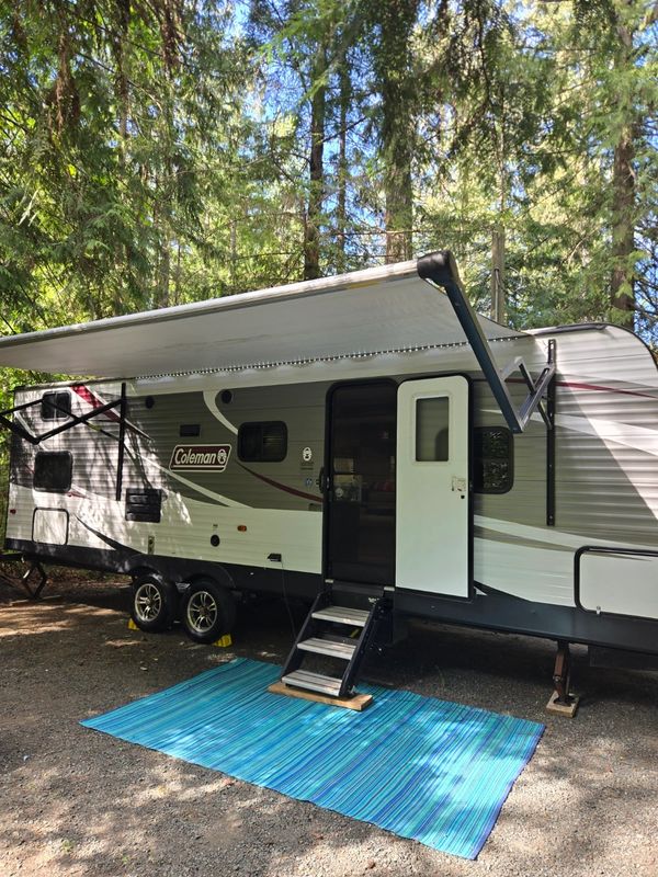 Coleman RV with awning in forest.