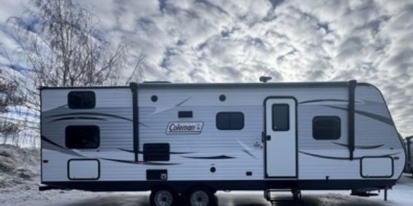 A Coleman travel trailer parked outdoors under a cloudy sky.