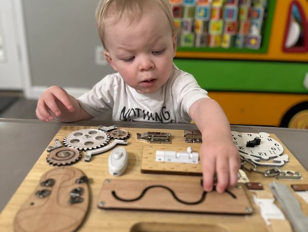 Toddler playing with a wooden activity board with gears and locks.