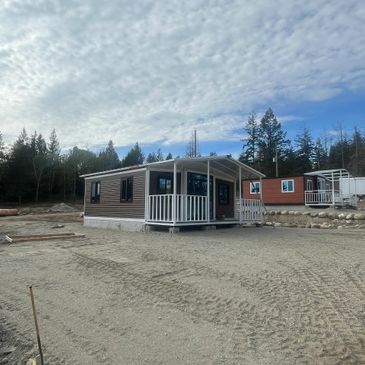 Small modern cabin with a porch in a clearing under a cloudy sky.