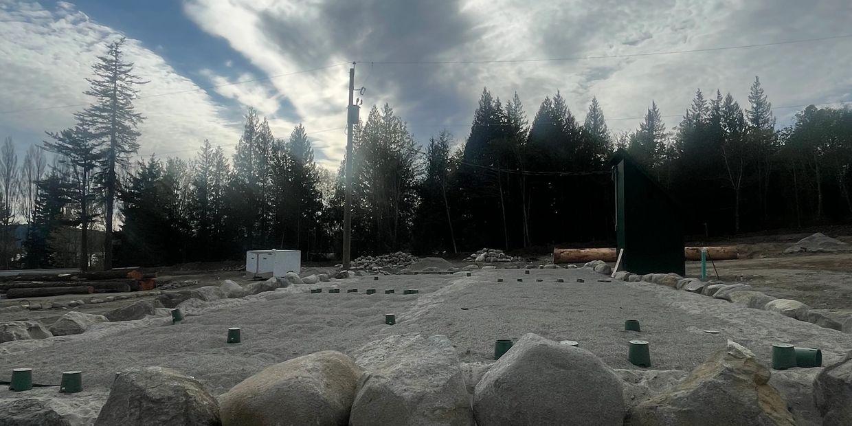 An outdoor bocce ball court surrounded by rocks and trees under a cloudy sky.
