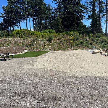 Empty gravel camping spot near forested area.