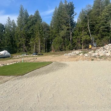 A gravel driveway leading to a forested area under a clear blue sky.