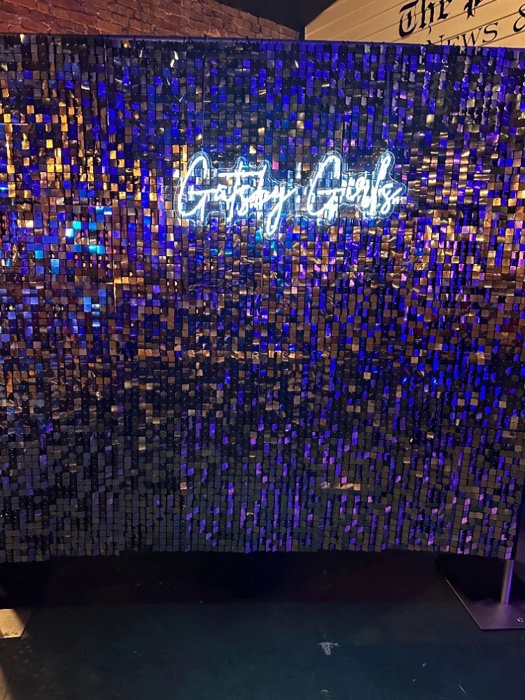 Shimmering sequin backdrop with glowing "Gatsby Girls" sign.