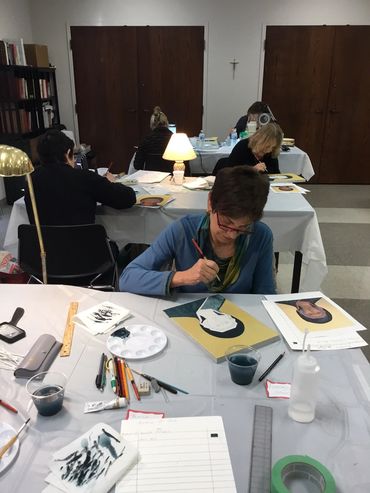 People painting portraits in a quiet studio with tables and art supplies.