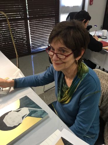 Woman with glasses sitting at a table drawing a portrait.