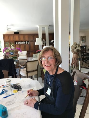 Woman smiling while drawing at a table in a well-lit room.
