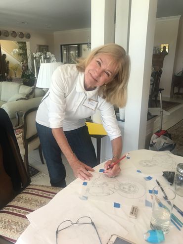 Woman sketching on paper at a table, smiling warmly.