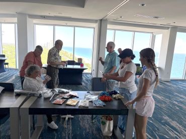 Group in a room with ocean view, examining items.