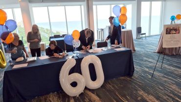 People signing a table with large '60' balloons.
