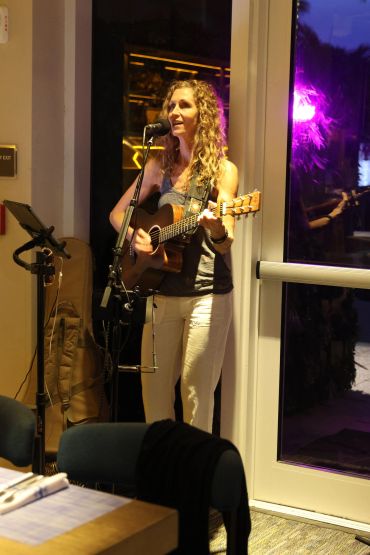 Woman performing live music with guitar indoors near a door.
