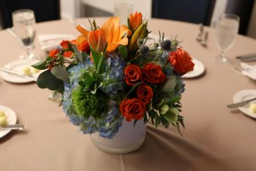 Elegant floral centerpiece with orange lilies and red roses on a banquet table.