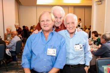 Three elderly men smiling at a social gathering with name badges.