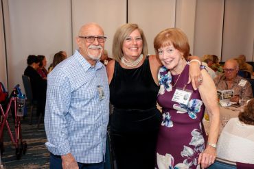 Three smiling adults posing at a social event indoors.