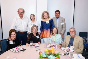 A group of eight older adults gathered around a table at a formal event.