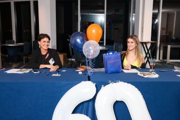 Two women sitting at a blue table with birthday balloons and a large '60' balloon decoration.