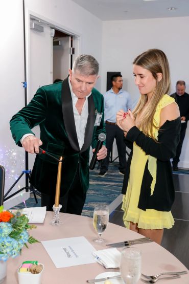 Man in green velvet jacket lights candle while woman in yellow dress watches.